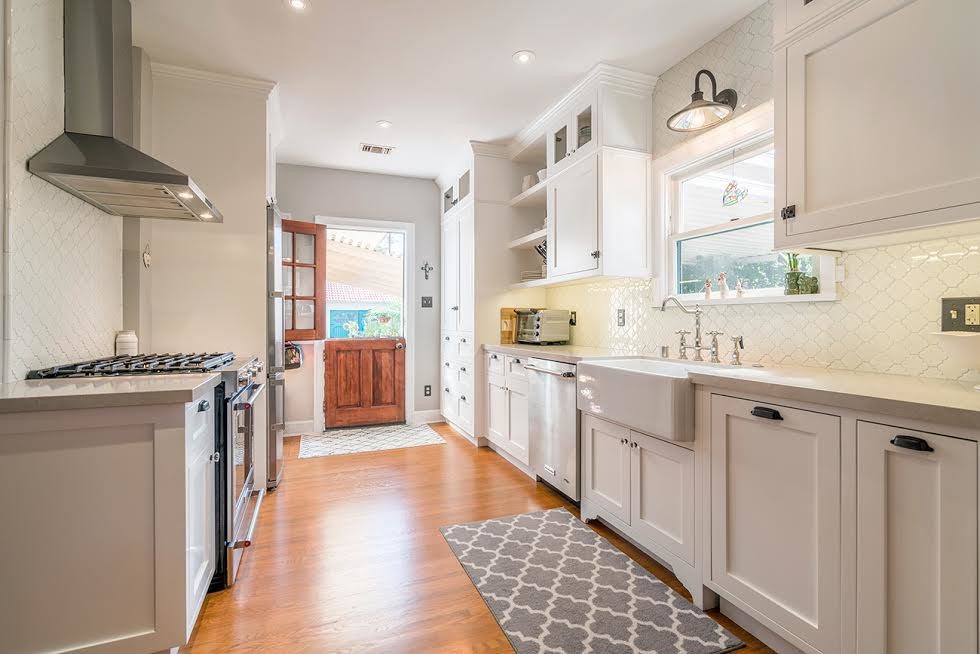 Design ideas for a small traditional single-wall kitchen pantry in Orange County with a belfast sink, shaker cabinets, white cabinets, engineered stone countertops, white splashback, ceramic splashback, stainless steel appliances, light hardwood flooring, no island and beige floors.