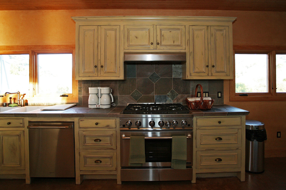 Exempel på ett mycket stort lantligt kök, med en nedsänkt diskho, luckor med upphöjd panel, skåp i slitet trä, kaklad bänkskiva, grått stänkskydd, stänkskydd i stenkakel, rostfria vitvaror, betonggolv och en köksö