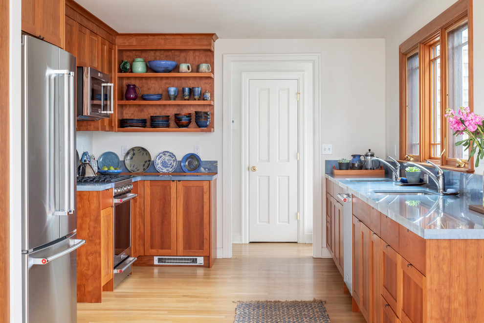 Klassisk inredning av ett mellanstort blå blått kök, med en undermonterad diskho, skåp i shakerstil, skåp i mellenmörkt trä, granitbänkskiva, blått stänkskydd, stänkskydd i sten, rostfria vitvaror och ljust trägolv