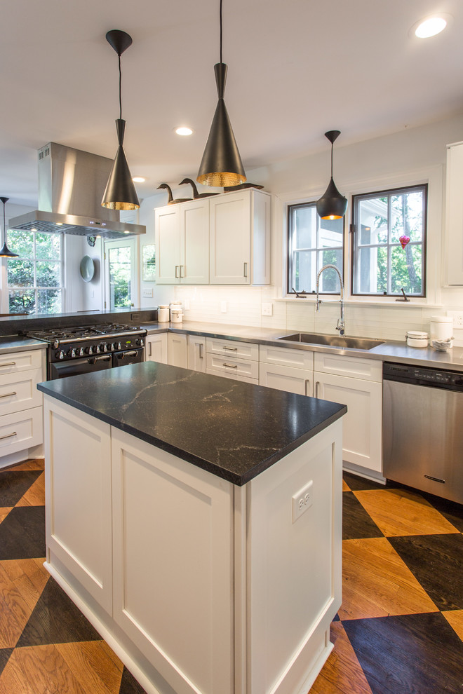 Minimalist light wood floor and multicolored floor enclosed kitchen photo in Raleigh with shaker cabinets, white cabinets, stainless steel countertops, white backsplash, subway tile backsplash, stainless steel appliances, an island and black countertops