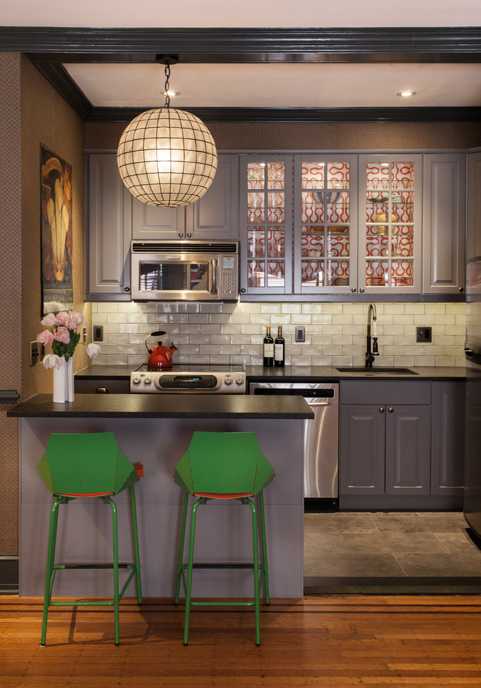 Inspiration for a transitional kitchen remodel in Philadelphia with an undermount sink, glass-front cabinets, gray cabinets, white backsplash, subway tile backsplash, stainless steel appliances and a peninsula