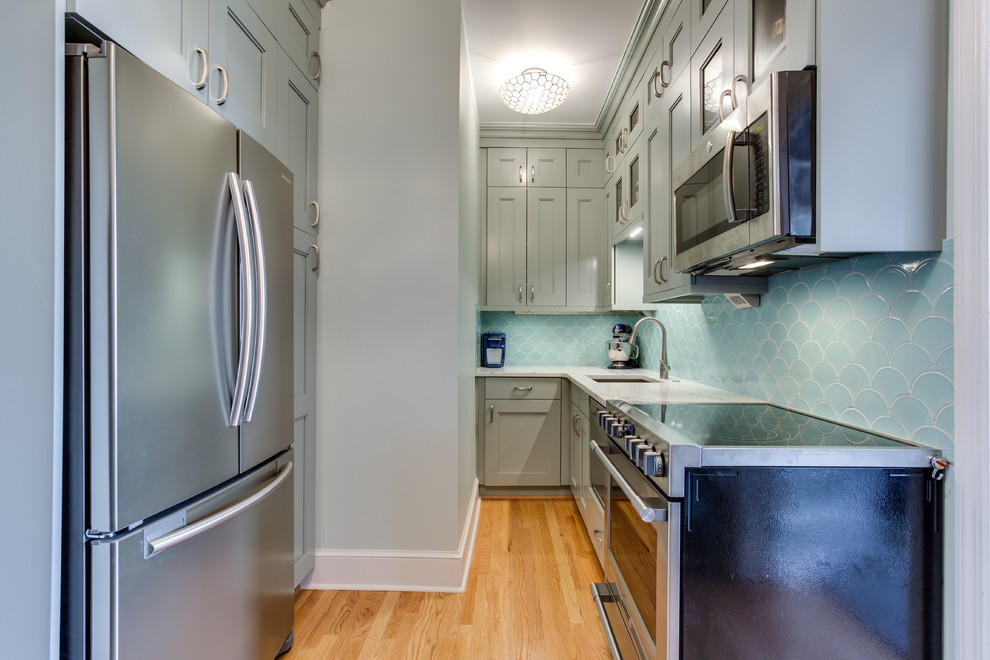 This is an example of a small classic kitchen/diner in DC Metro with a single-bowl sink, shaker cabinets, blue cabinets, engineered stone countertops, blue splashback, ceramic splashback, stainless steel appliances, light hardwood flooring and no island.