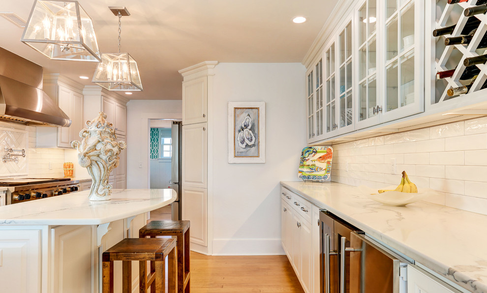 Example of a large beach style light wood floor open concept kitchen design in Wilmington with white cabinets, marble countertops, white backsplash, porcelain backsplash, stainless steel appliances and an island
