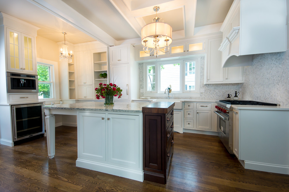 Inredning av ett klassiskt mellanstort kök, med en rustik diskho, luckor med infälld panel, vita skåp, granitbänkskiva, grått stänkskydd, stänkskydd i glaskakel, rostfria vitvaror, mörkt trägolv, en köksö och brunt golv