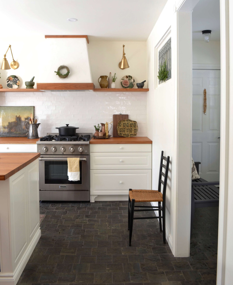 トロントにあるカントリー風のおしゃれなキッチン (ヴィンテージ仕上げキャビネット、木材カウンター、白いキッチンパネル、サブウェイタイルのキッチンパネル、シルバーの調理設備、黒い床、茶色いキッチンカウンター) の写真