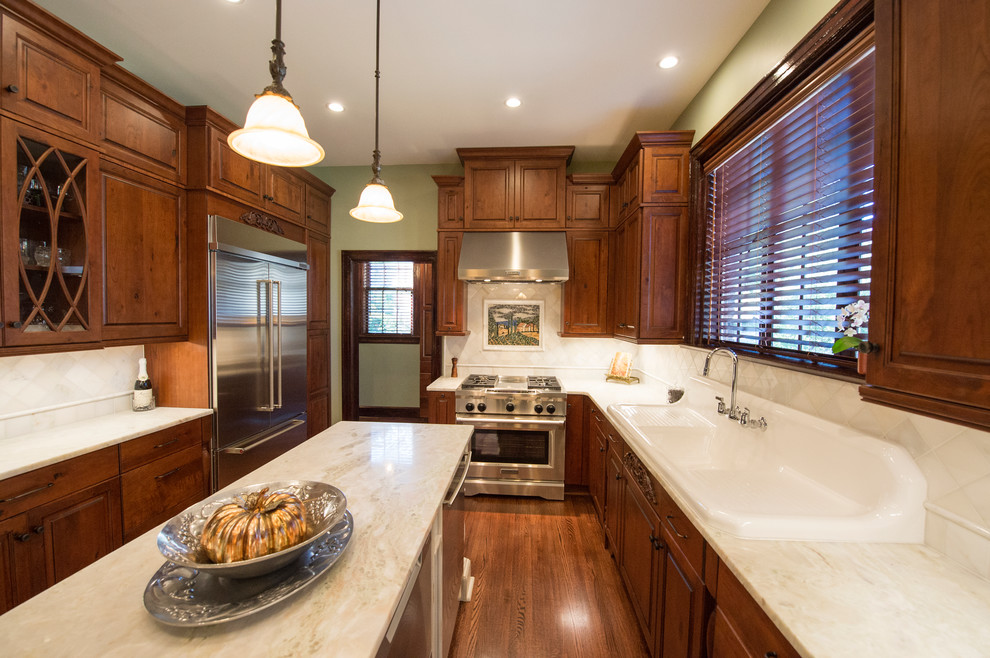 Exempel på ett stort klassiskt kök, med en rustik diskho, luckor med upphöjd panel, skåp i mörkt trä, bänkskiva i onyx, vitt stänkskydd, stänkskydd i stenkakel, rostfria vitvaror, mellanmörkt trägolv och en köksö