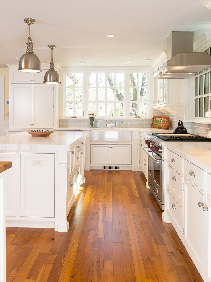 Inredning av ett lantligt kök, med luckor med infälld panel, vita skåp, marmorbänkskiva, grått stänkskydd, stänkskydd i glaskakel, rostfria vitvaror och en köksö
