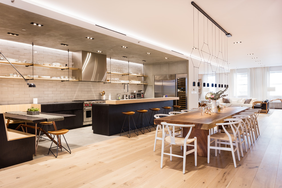 Imagen de cocina industrial abierta con armarios abiertos, salpicadero blanco, electrodomésticos de acero inoxidable, suelo de madera clara y barras de cocina