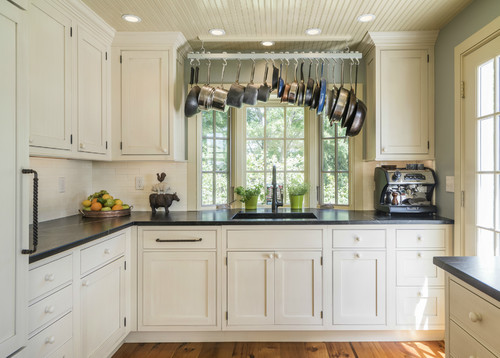 Bright Canadian kitchen with classic off-white shaker cabinets, black countertops, stainless steel hanging pots, and natural light from large windows, representing one of the best kitchen cabinet color choices in Canada.