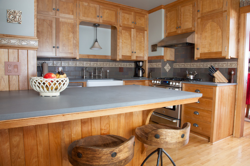 Example of a mid-sized arts and crafts l-shaped light wood floor and brown floor eat-in kitchen design in Minneapolis with a farmhouse sink, medium tone wood cabinets, soapstone countertops, gray backsplash, ceramic backsplash, stainless steel appliances, recessed-panel cabinets and a peninsula