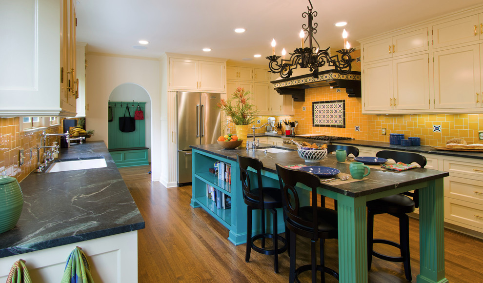 Medelhavsstil inredning av ett stort u-kök, med en undermonterad diskho, luckor med infälld panel, vita skåp, bänkskiva i täljsten, gult stänkskydd, stänkskydd i mosaik, rostfria vitvaror, mellanmörkt trägolv, en köksö och brunt golv