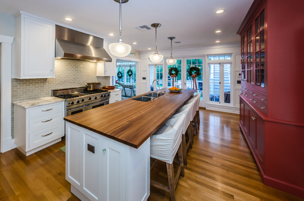 Example of a classic galley medium tone wood floor and brown floor kitchen design in Tampa with an undermount sink, shaker cabinets, white cabinets, wood countertops, gray backsplash, subway tile backsplash, stainless steel appliances, an island and brown countertops