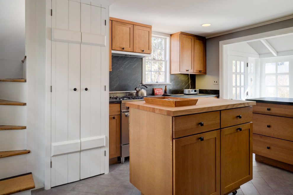 Réalisation d'une cuisine champêtre en bois clair avec un placard à porte shaker, une crédence noire, un électroménager en acier inoxydable, 2 îlots, un sol gris et plan de travail noir.