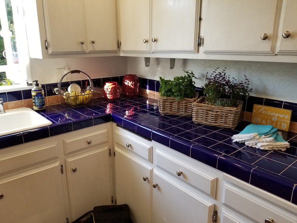 This is an example of a small nautical u-shaped enclosed kitchen in Baltimore with a double-bowl sink, flat-panel cabinets, white cabinets, tile countertops, blue splashback, ceramic splashback, stainless steel appliances, medium hardwood flooring, no island, brown floors and blue worktops.