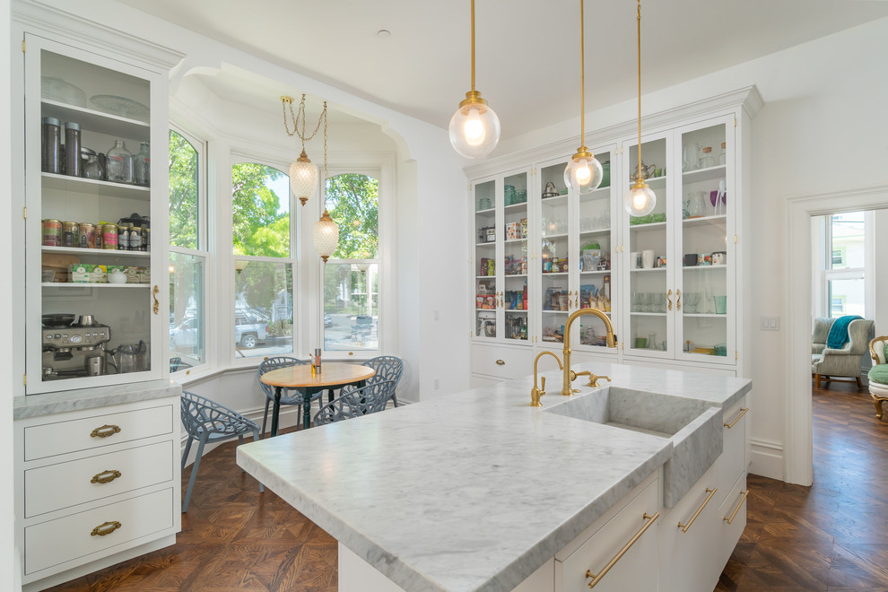 Klassische Küche mit Landhausspüle, Schrankfronten mit vertiefter Füllung, Marmor-Arbeitsplatte, Küchenrückwand in Weiß, Rückwand aus Marmor, braunem Holzboden, Kücheninsel und weißer Arbeitsplatte in San Francisco