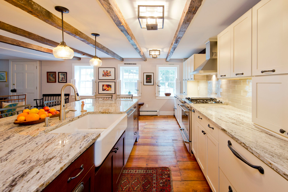 Mid-sized transitional single-wall light wood floor and brown floor enclosed kitchen photo in DC Metro with a farmhouse sink, shaker cabinets, white cabinets, granite countertops, white backsplash, glass tile backsplash, stainless steel appliances and an island