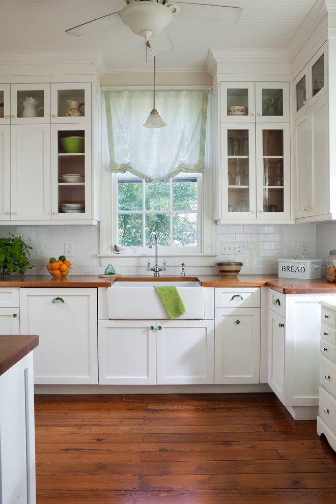 Example of a classic kitchen design in Wilmington with glass-front cabinets, a farmhouse sink, wood countertops, white cabinets, white backsplash and subway tile backsplash