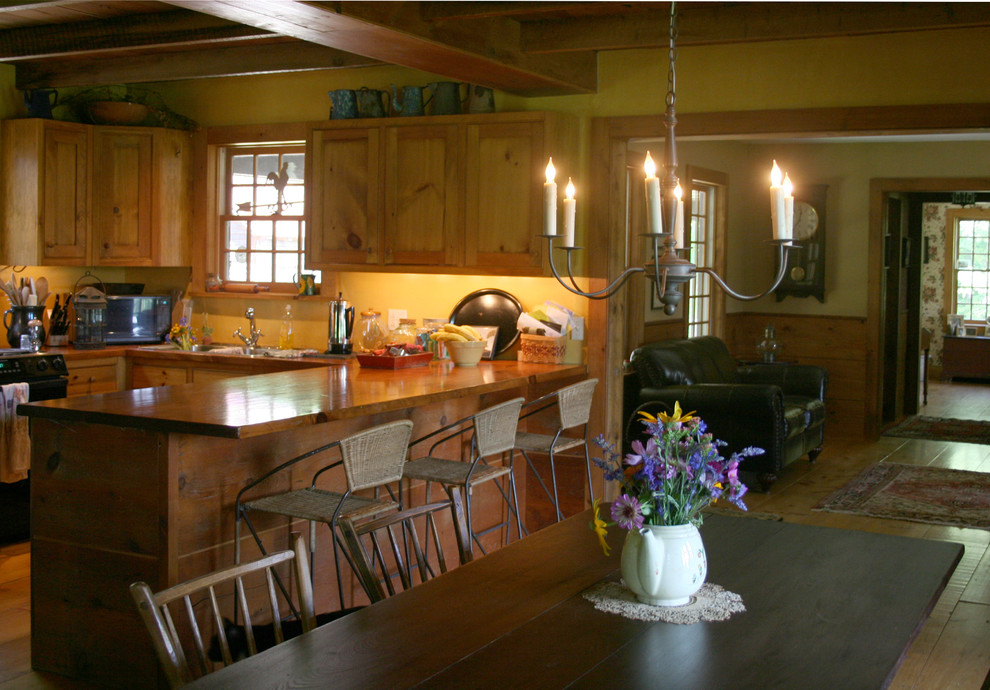 Immagine di una cucina ad U country con ante con riquadro incassato, ante in legno chiaro, top in legno, paraspruzzi giallo, elettrodomestici neri e parquet chiaro