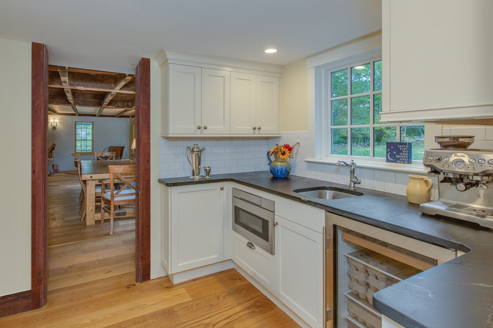 Bild på ett mellanstort lantligt kök, med en rustik diskho, luckor med infälld panel, vita skåp, bänkskiva i täljsten, vitt stänkskydd, stänkskydd i tunnelbanekakel, integrerade vitvaror, mellanmörkt trägolv, en köksö och brunt golv