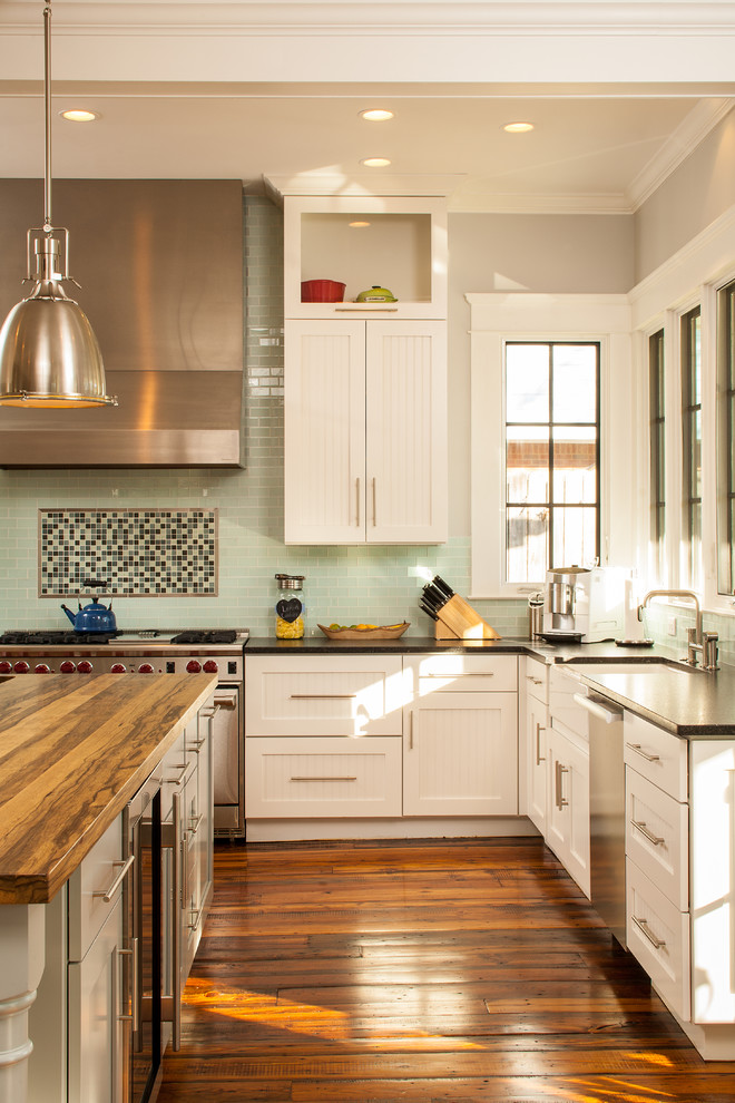 На фото: кухня в стиле кантри с фасадами в стиле шейкер, белыми фасадами, деревянной столешницей, зеленым фартуком, фартуком из стеклянной плитки, окном и красивой плиткой