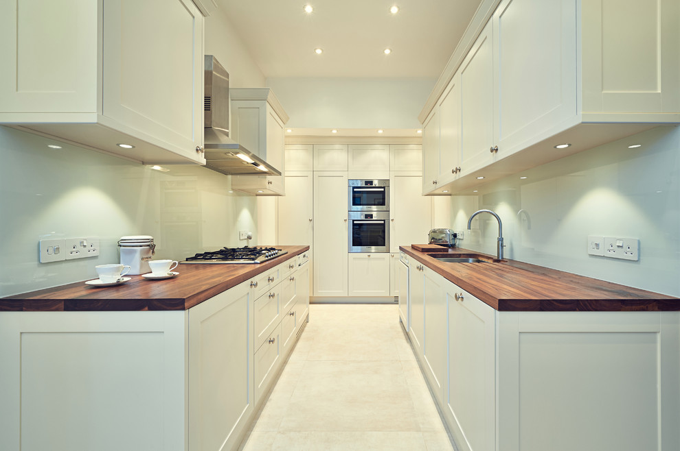 ロンドンにある高級な小さなコンテンポラリースタイルのおしゃれなキッチン (一体型シンク、シェーカースタイル扉のキャビネット、白いキャビネット、木材カウンター、白いキッチンパネル、ガラス板のキッチンパネル、シルバーの調理設備、磁器タイルの床) の写真