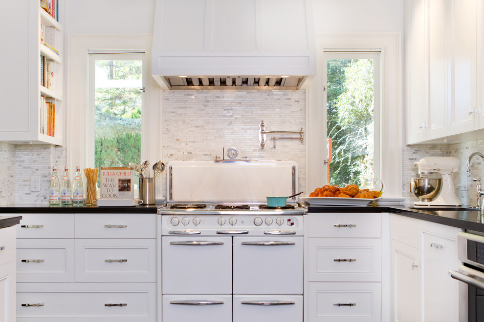 Example of a transitional kitchen design in Los Angeles with recessed-panel cabinets, white appliances, stone tile backsplash and white cabinets