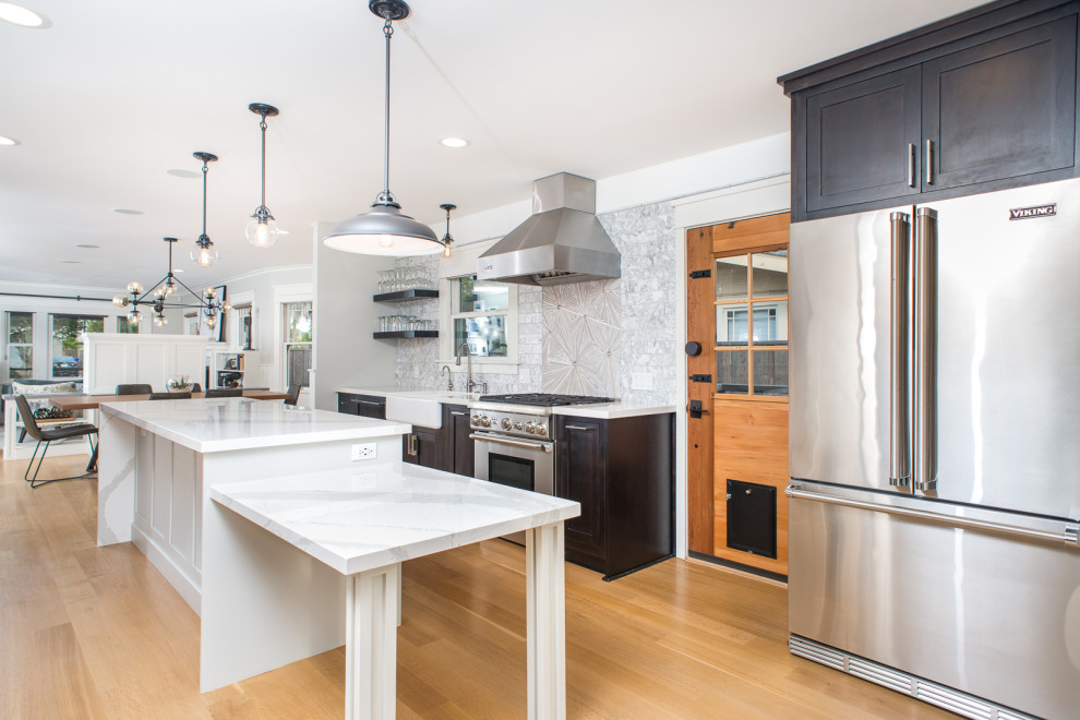Mid-sized transitional light wood floor and brown floor enclosed kitchen photo with a farmhouse sink, shaker cabinets, black cabinets, quartzite countertops, gray backsplash, mosaic tile backsplash, stainless steel appliances, an island and gray countertops