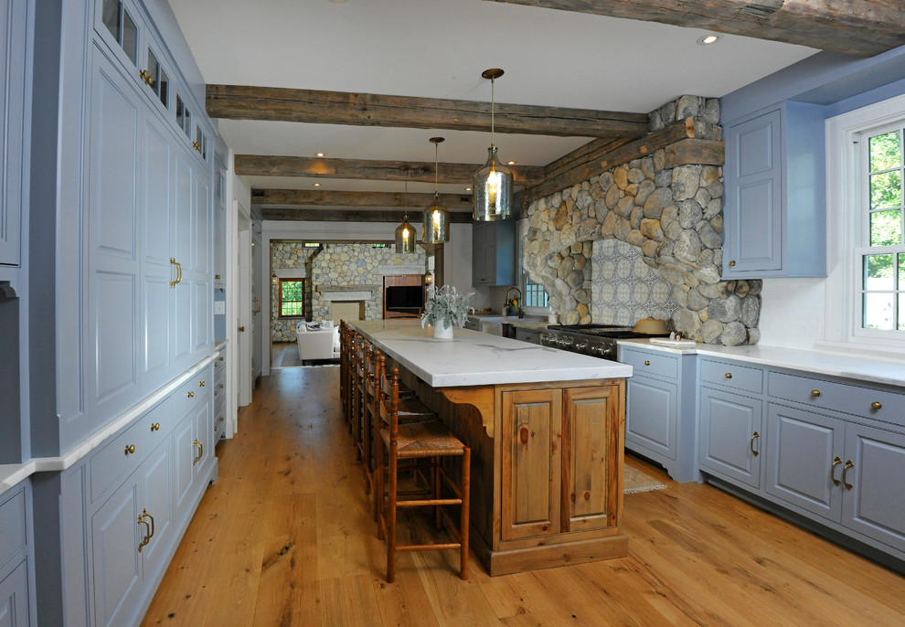 Cette image montre une cuisine parallèle chalet avec un placard avec porte à panneau surélevé, des portes de placard bleues, une crédence bleue, un sol en bois brun, îlot et un sol marron.