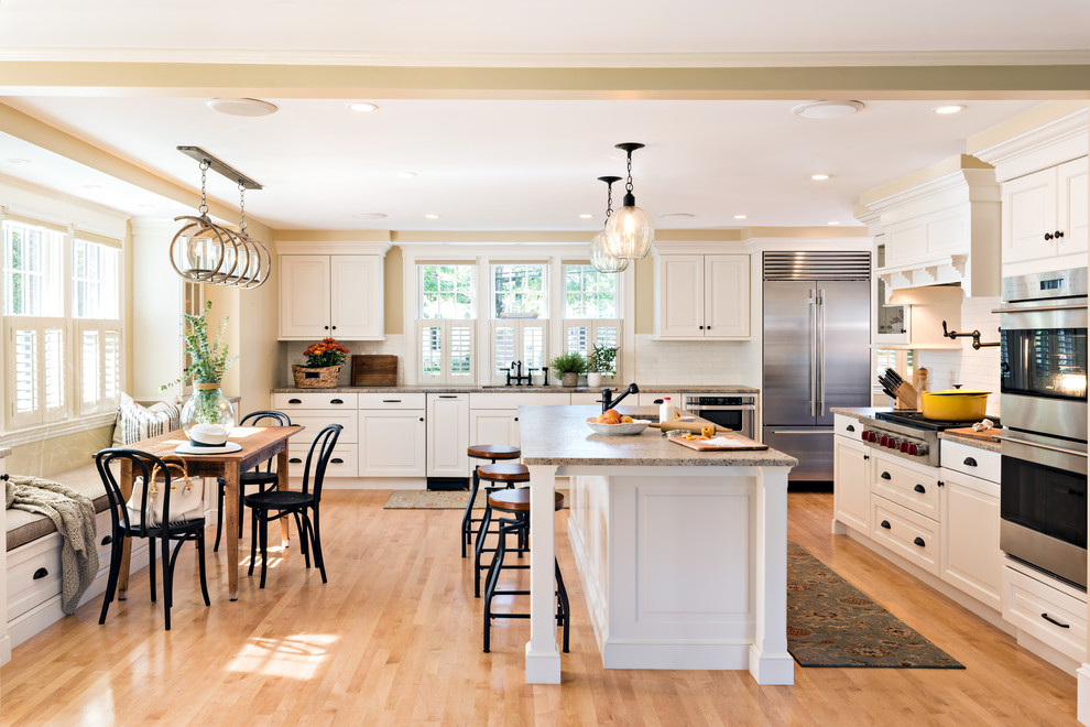 Klassische Wohnküche in L-Form mit Unterbauwaschbecken, profilierten Schrankfronten, weißen Schränken, Küchenrückwand in Weiß, Küchengeräten aus Edelstahl, hellem Holzboden, Kücheninsel und braunem Boden in Boston