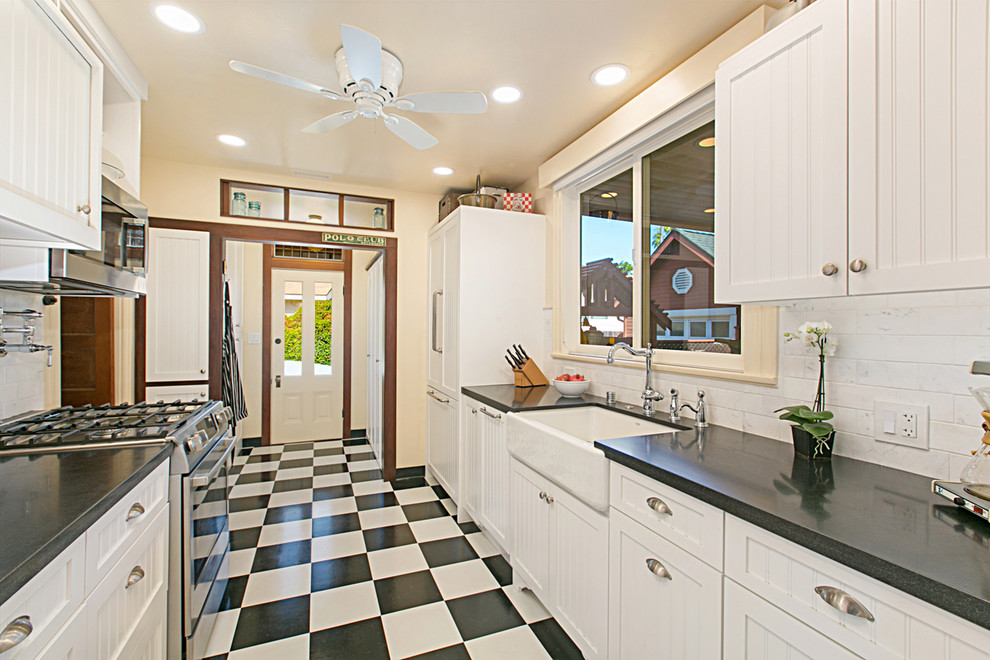 Foto på ett mellanstort vintage svart kök, med en rustik diskho, luckor med profilerade fronter, vita skåp, granitbänkskiva, vitt stänkskydd, stänkskydd i marmor, integrerade vitvaror, linoleumgolv och flerfärgat golv