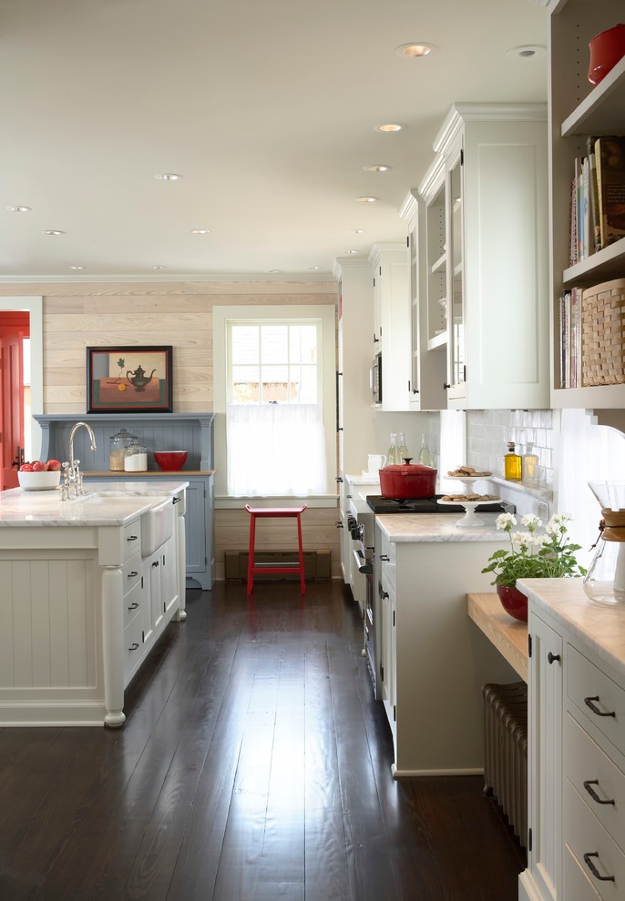 Design ideas for a small traditional galley open plan kitchen in Minneapolis with a belfast sink, recessed-panel cabinets, white cabinets, marble worktops, white splashback, ceramic splashback, white appliances, dark hardwood flooring and an island.