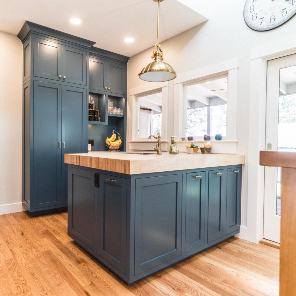 Inspiration for a large country galley kitchen/diner in Denver with a belfast sink, flat-panel cabinets, blue cabinets, white splashback, stainless steel appliances, light hardwood flooring, multiple islands, brown floors and white worktops.