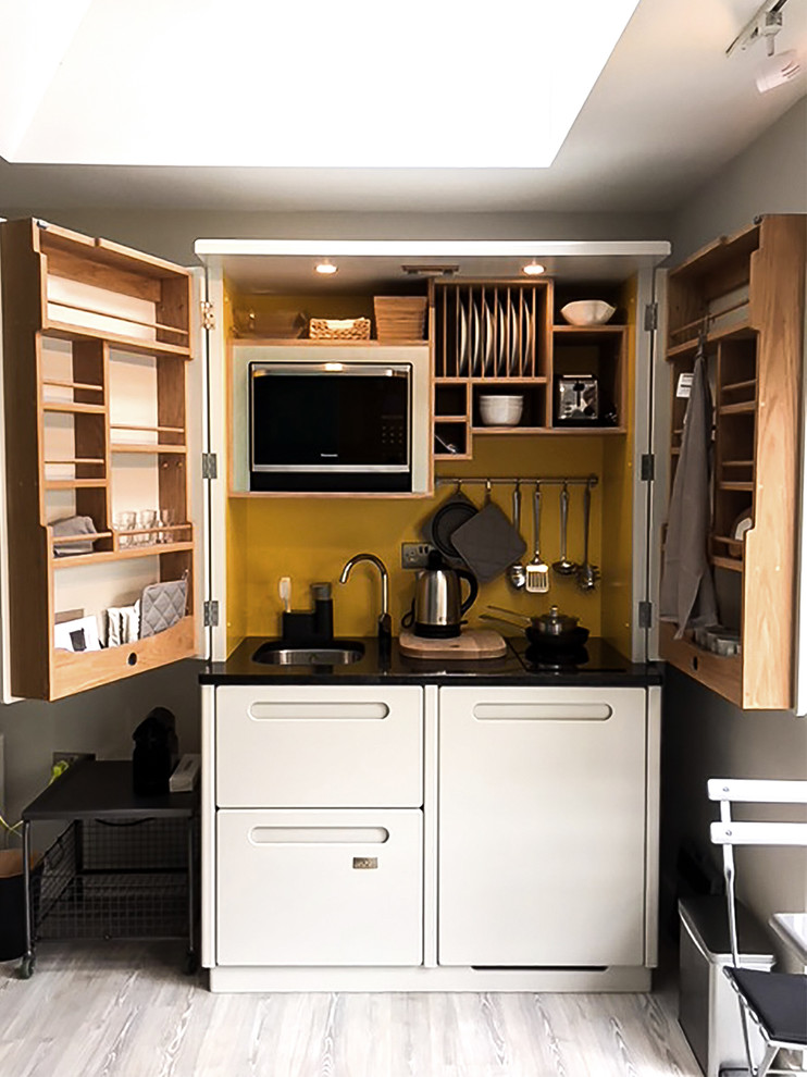 Idéer för att renovera ett litet 60 tals svart linjärt svart kök med öppen planlösning, med en nedsänkt diskho, släta luckor, grå skåp, granitbänkskiva, gult stänkskydd, stänkskydd i trä, rostfria vitvaror, laminatgolv och grått golv