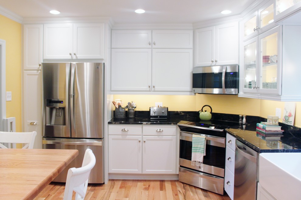 Foto på ett avskilt, mellanstort lantligt l-kök, med en rustik diskho, luckor med glaspanel, vita skåp, granitbänkskiva, gult stänkskydd, rostfria vitvaror, ljust trägolv och en köksö