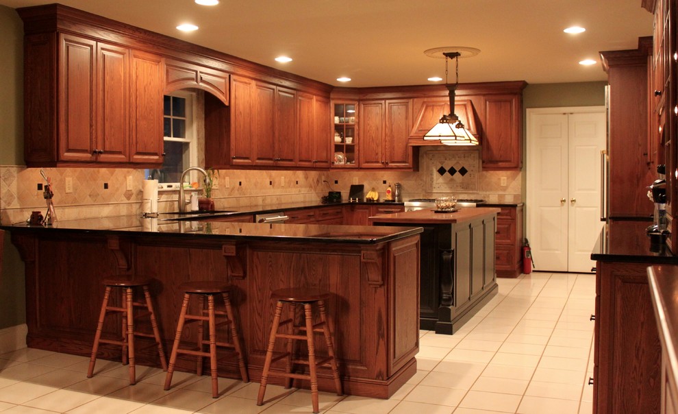 Klassisk inredning av ett stort kök, med en undermonterad diskho, luckor med upphöjd panel, skåp i mellenmörkt trä, granitbänkskiva, beige stänkskydd, stänkskydd i stenkakel, rostfria vitvaror, klinkergolv i porslin och en köksö