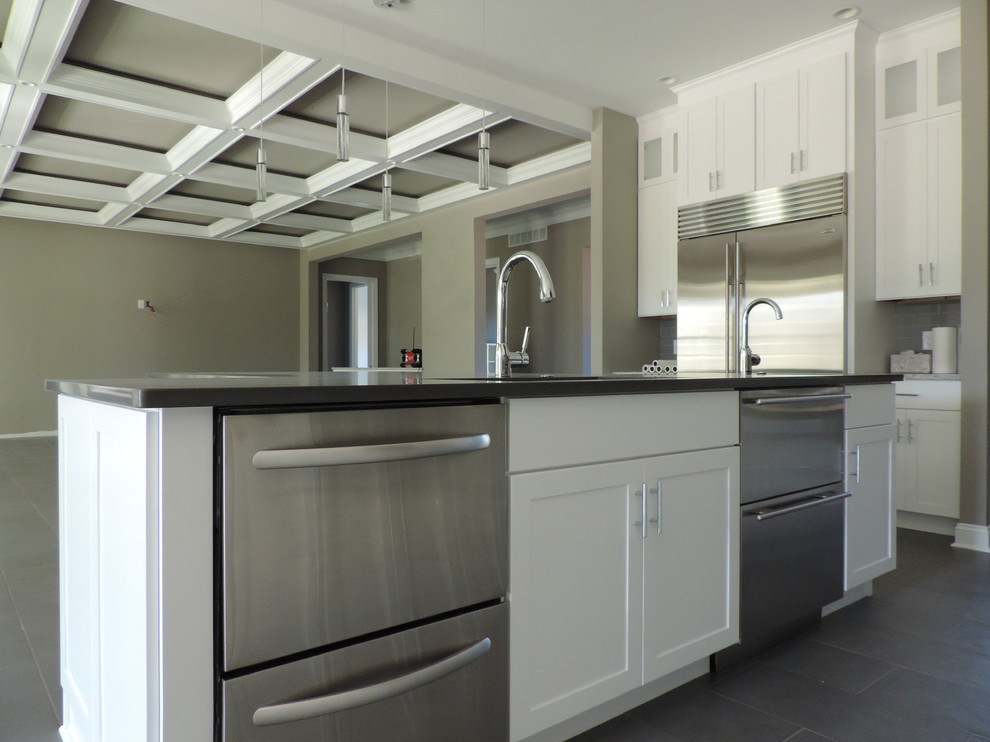 Example of a large trendy l-shaped gray floor eat-in kitchen design in Philadelphia with white cabinets, gray backsplash, stainless steel appliances, an island, an undermount sink, shaker cabinets, subway tile backsplash and black countertops