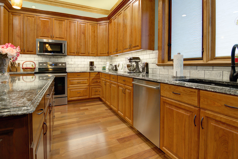 Große Klassische Küche mit Unterbauwaschbecken, profilierten Schrankfronten, hellbraunen Holzschränken, Granit-Arbeitsplatte, Küchengeräten aus Edelstahl, braunem Holzboden, Kücheninsel und braunem Boden in Chicago
