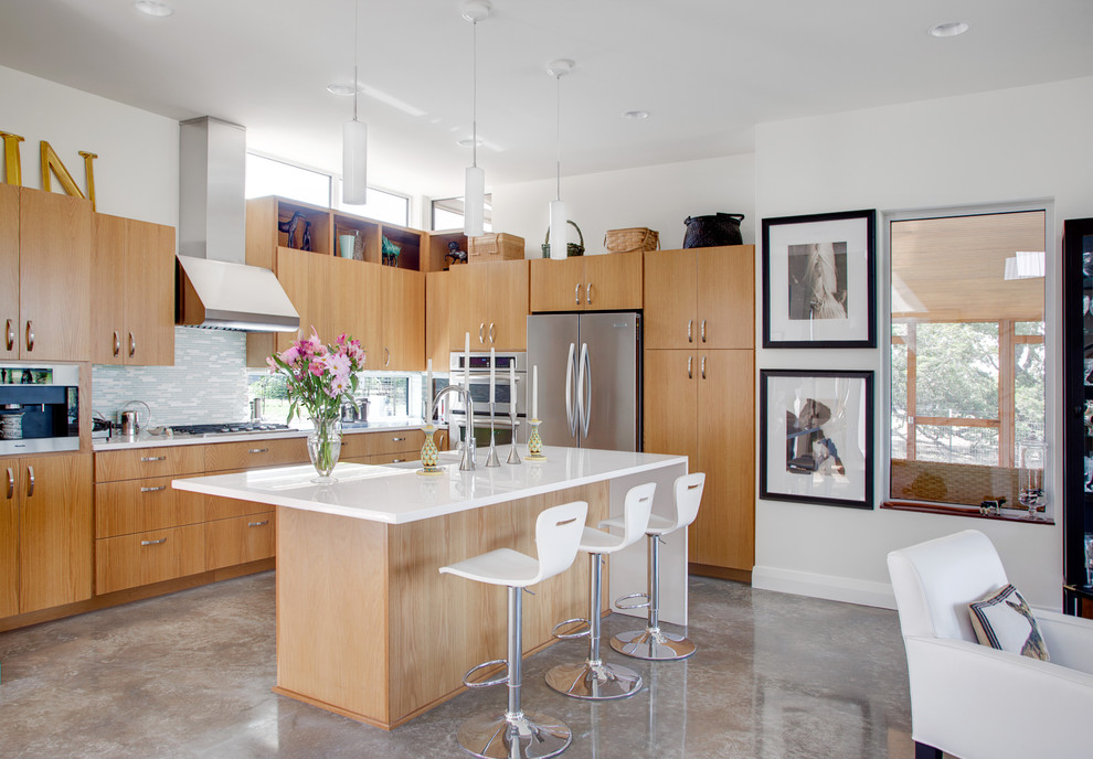 На фото: п-образная кухня-гостиная в современном стиле с плоскими фасадами, серым фартуком, техникой из нержавеющей стали, светлыми деревянными фасадами, бетонным полом и серым полом