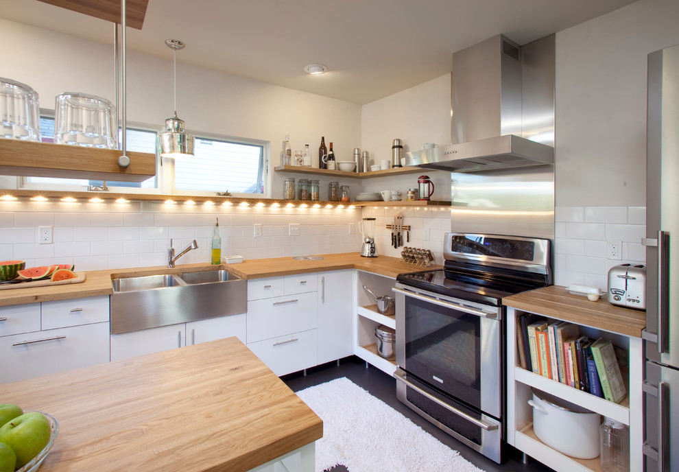 Example of a mid-sized minimalist u-shaped kitchen design in Portland with a farmhouse sink, flat-panel cabinets, white cabinets, wood countertops, white backsplash, subway tile backsplash and stainless steel appliances