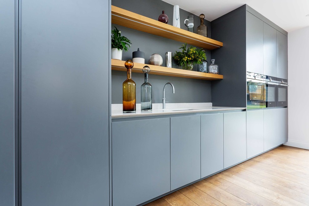 This is an example of a medium sized contemporary single-wall kitchen in London with flat-panel cabinets, stainless steel appliances, light hardwood flooring and an island.