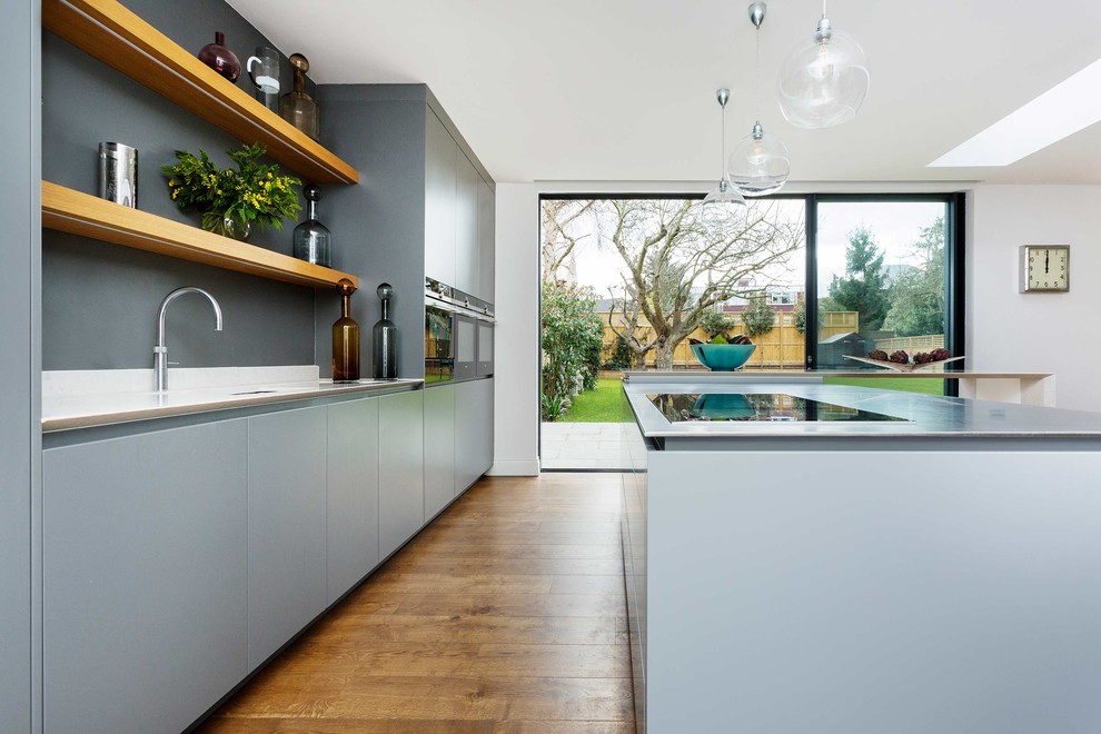 Design ideas for a medium sized contemporary single-wall kitchen in London with flat-panel cabinets, stainless steel appliances, light hardwood flooring and an island.