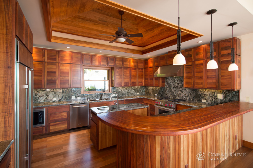 ハワイにあるラグジュアリーな広いトロピカルスタイルのおしゃれなキッチン (アンダーカウンターシンク、中間色木目調キャビネット、御影石カウンター、マルチカラーのキッチンパネル、石スラブのキッチンパネル、シルバーの調理設備、淡色無垢フローリング) の写真
