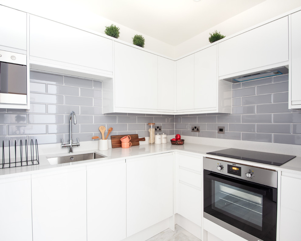 Photo of a scandinavian l-shaped kitchen in London with a submerged sink, flat-panel cabinets, white cabinets, grey splashback, stainless steel appliances, no island, grey floors and white worktops.
