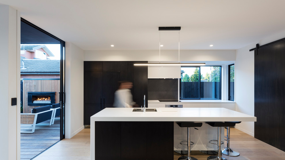 Immagine di un cucina con isola centrale minimal di medie dimensioni con lavello sottopiano, ante lisce, ante nere, paraspruzzi a finestra, parquet chiaro e pavimento beige