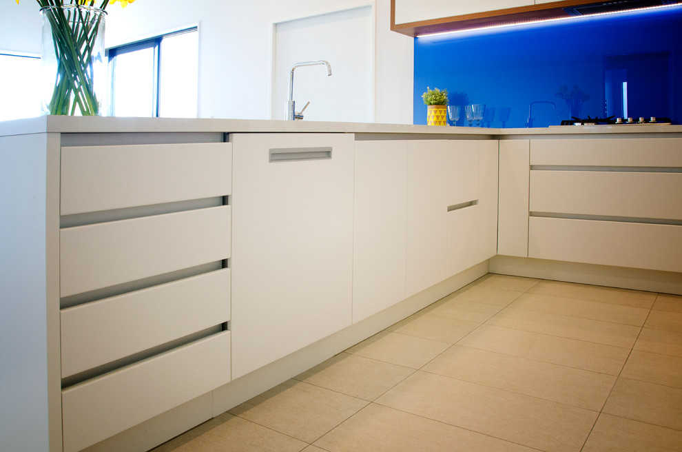 Exempel på ett mellanstort modernt vit vitt kök, med en enkel diskho, släta luckor, vita skåp, laminatbänkskiva, blått stänkskydd, glaspanel som stänkskydd, rostfria vitvaror, klinkergolv i keramik, en halv köksö och beiget golv