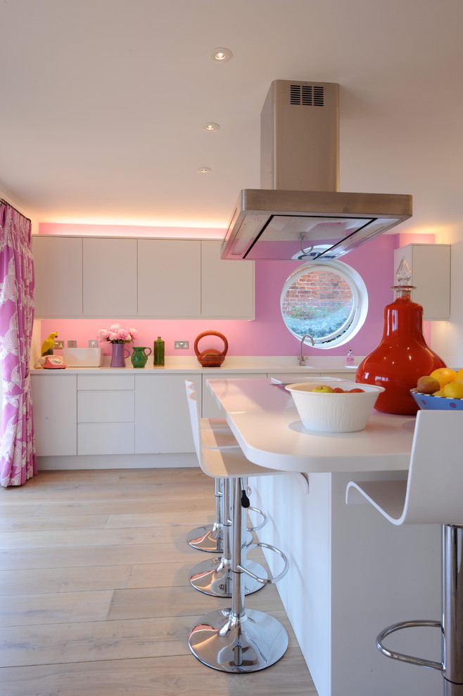 На фото: кухня в современном стиле с врезной мойкой, плоскими фасадами, белыми фасадами, розовым фартуком и светлым паркетным полом с