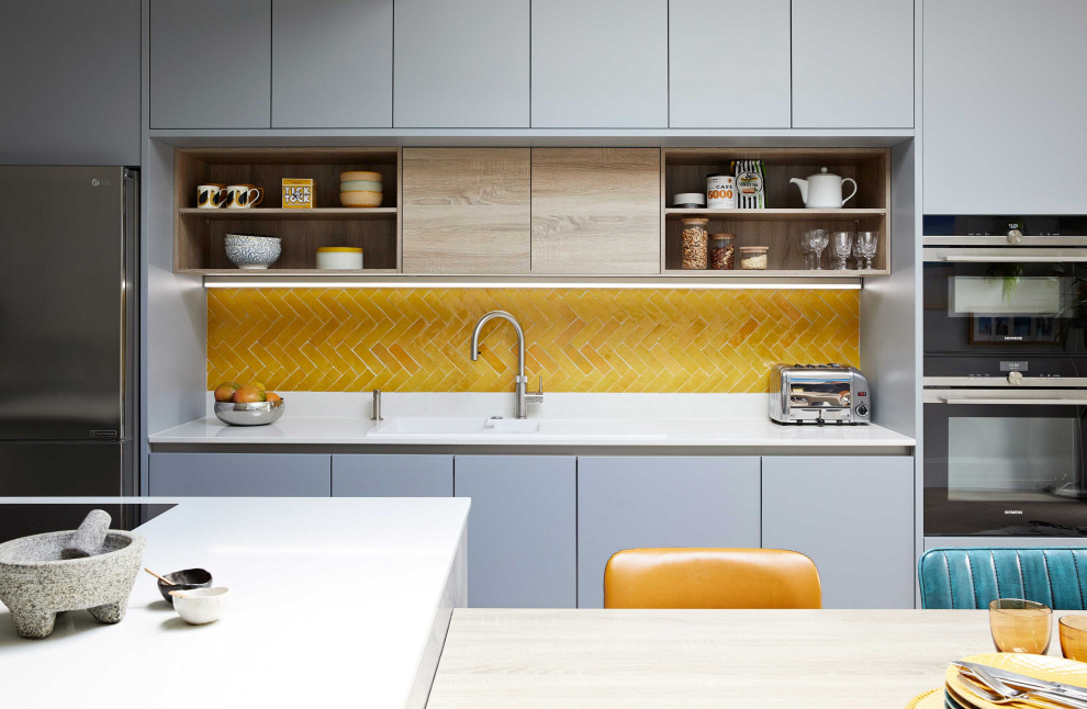 Example of a large trendy eat-in kitchen design in London with flat-panel cabinets, gray cabinets, quartzite countertops, yellow backsplash, ceramic backsplash, an island and white countertops