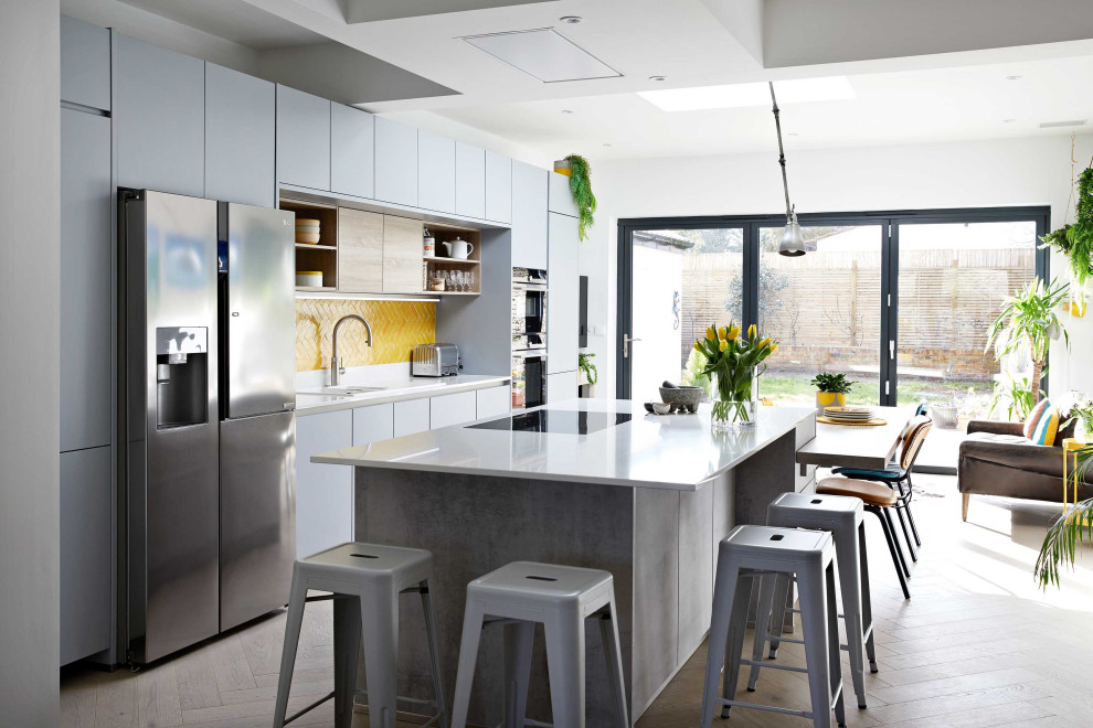 Bild på ett stort funkis vit vitt kök och matrum, med släta luckor, grå skåp, bänkskiva i kvartsit, gult stänkskydd, stänkskydd i keramik och en köksö