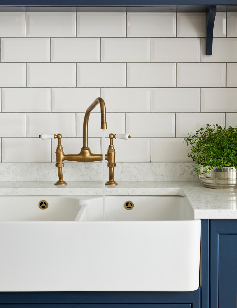 Kitchen - mid-sized transitional kitchen idea in Sussex with a farmhouse sink, white backsplash, subway tile backsplash, stainless steel appliances and an island