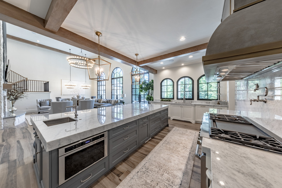 Example of a large tuscan porcelain tile and brown floor open concept kitchen design in Salt Lake City with an undermount sink, recessed-panel cabinets, white cabinets, marble countertops, gray backsplash, marble backsplash, paneled appliances and an island